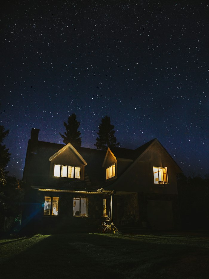 Two-story house with soft roofline and window lighting under a night sky